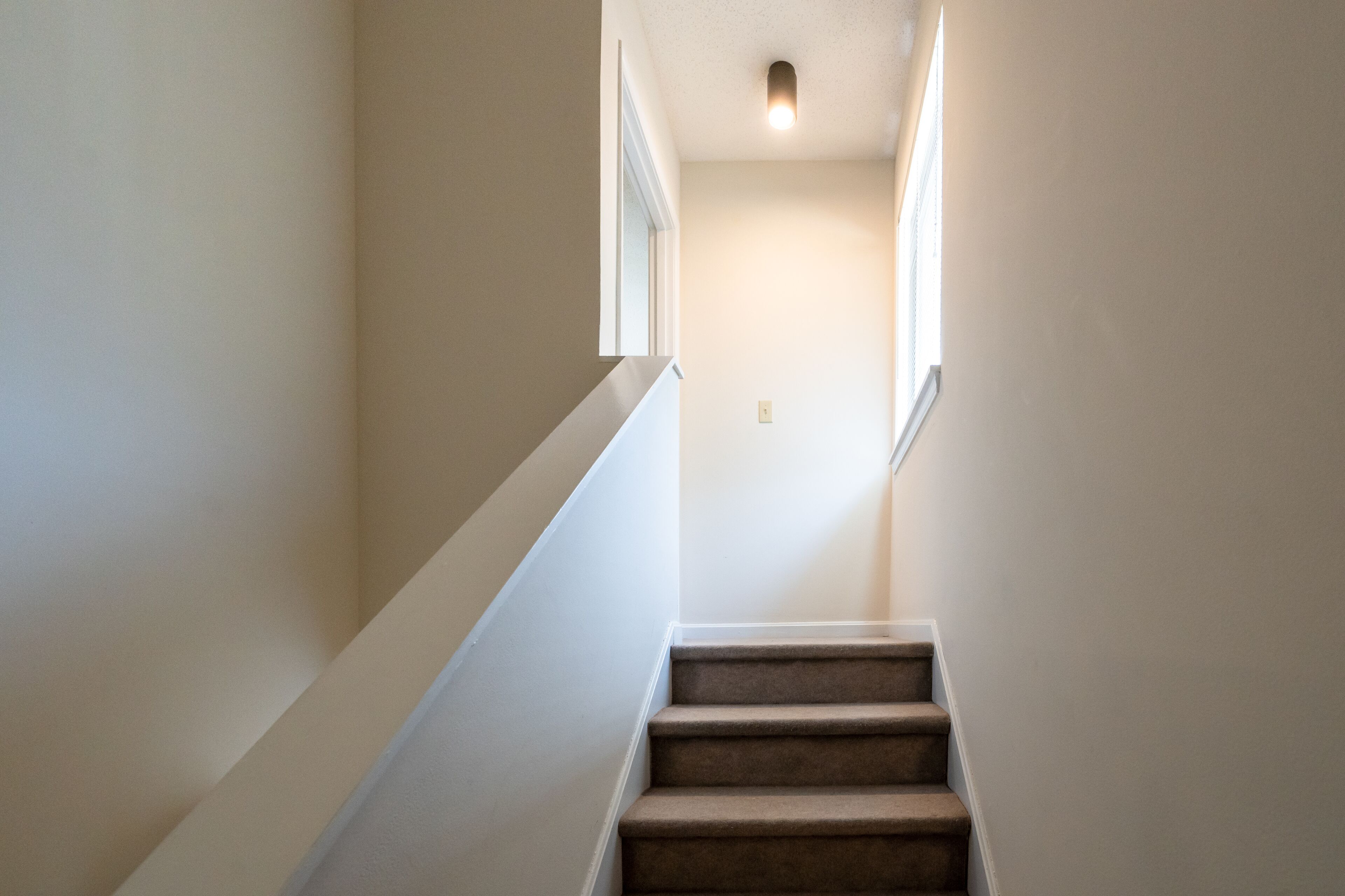 Eine enge Treppe mit einer Teppichstufenplattform und weißen Wänden.