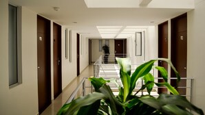 Ein moderner Hotelkorridor mit einer zentralen Treppe, Holztüren und einem Blumentopf im Vordergrund.