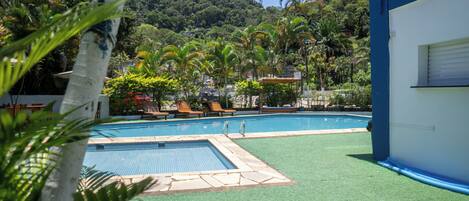Piscina con zona de césped artificial verde, rodeada de palmeras y con montañas al fondo.