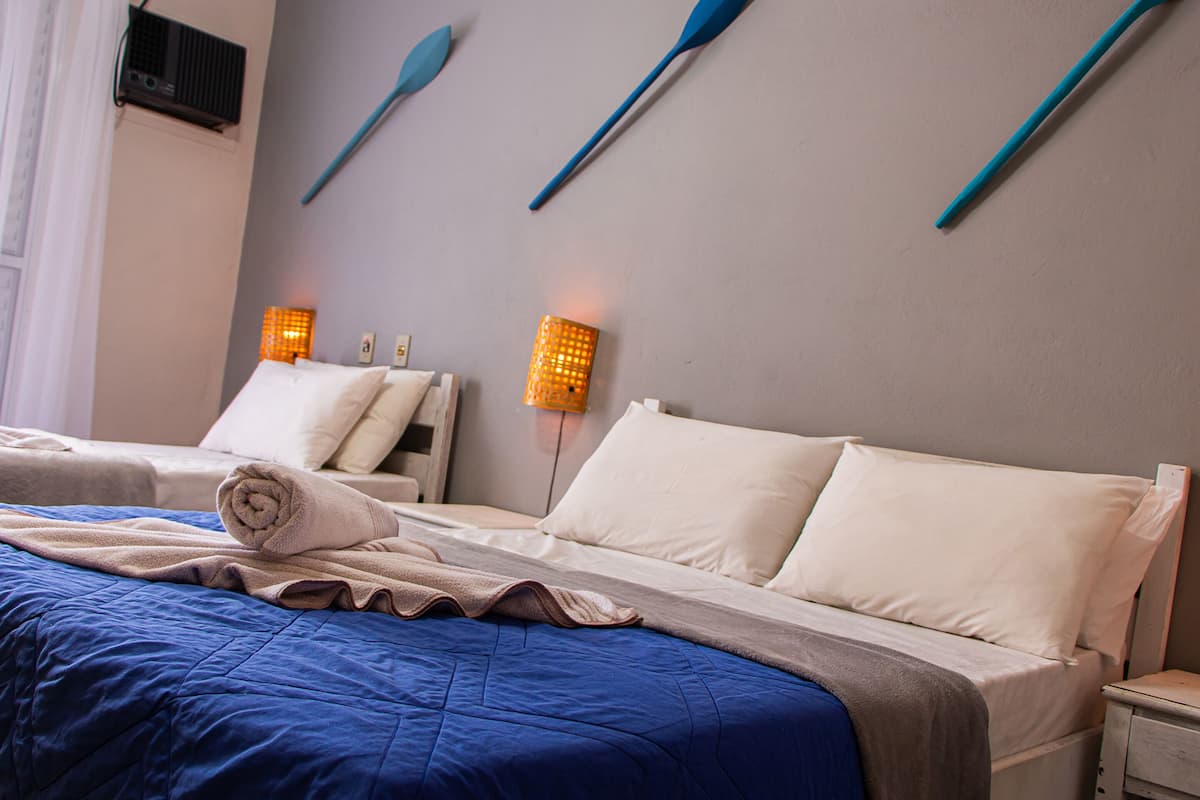 Habitación de hotel con dos camas, una colcha azul, almohadas blancas y dos lámparas fijadas a la pared.