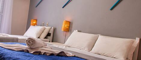 A hotel room with two beds, a blue bedspread, white pillows, and two wall-mounted lamps.