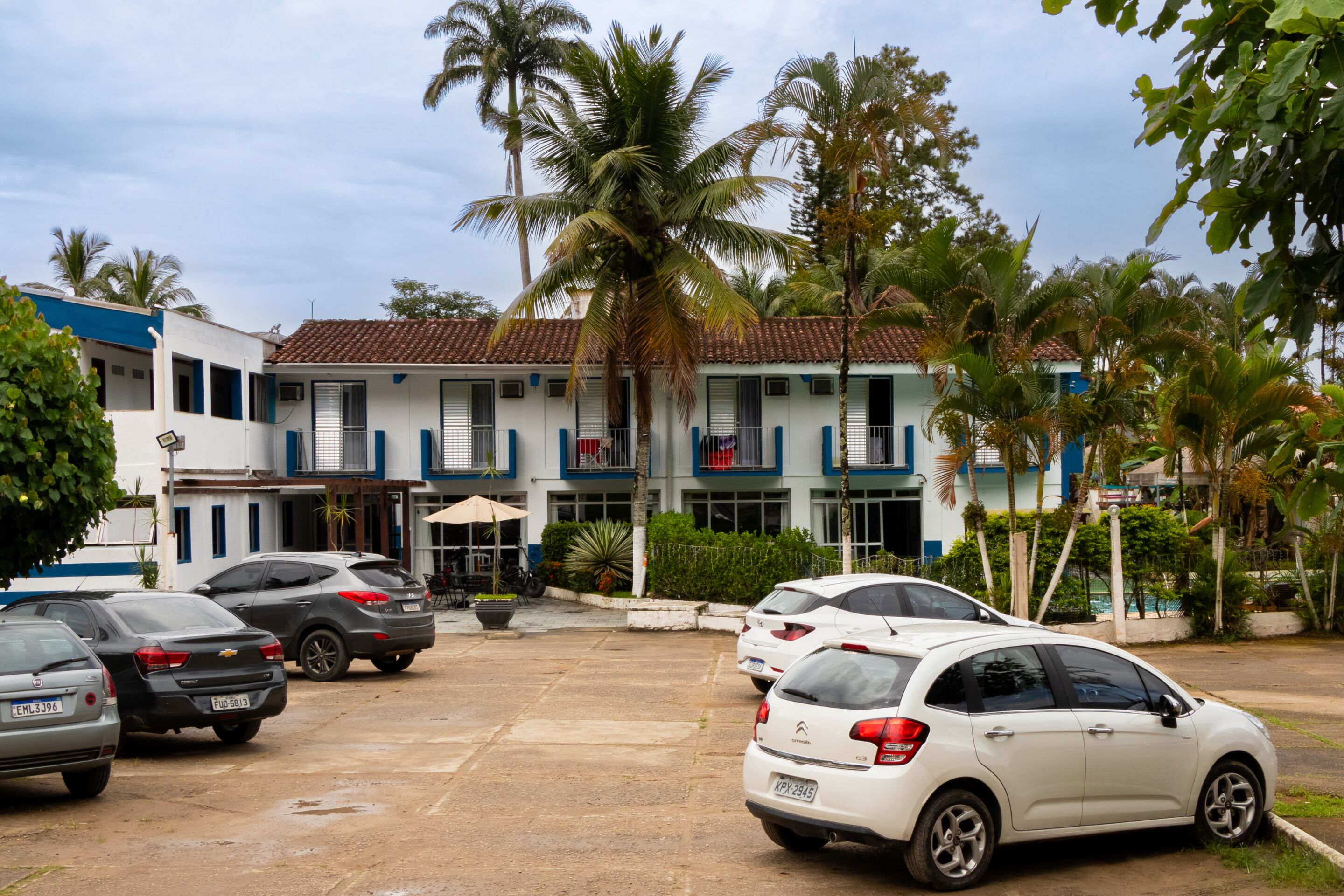 A parking lot with several cars, a building with a tiled roof, and palm trees.