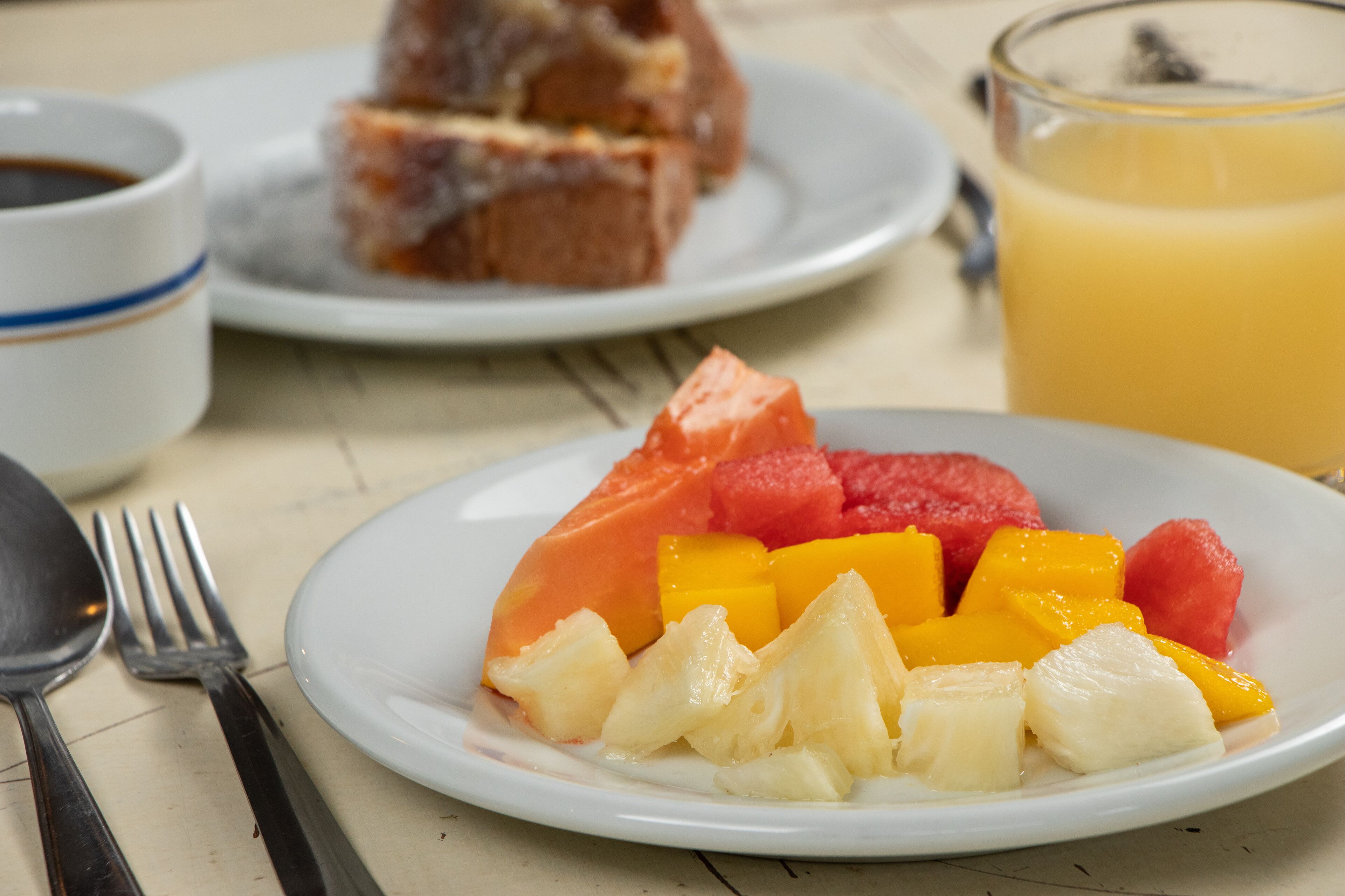 Ein Teller mit Früchten, ein Glas Orangensaft und ein Stück Kuchen auf einem Tisch.