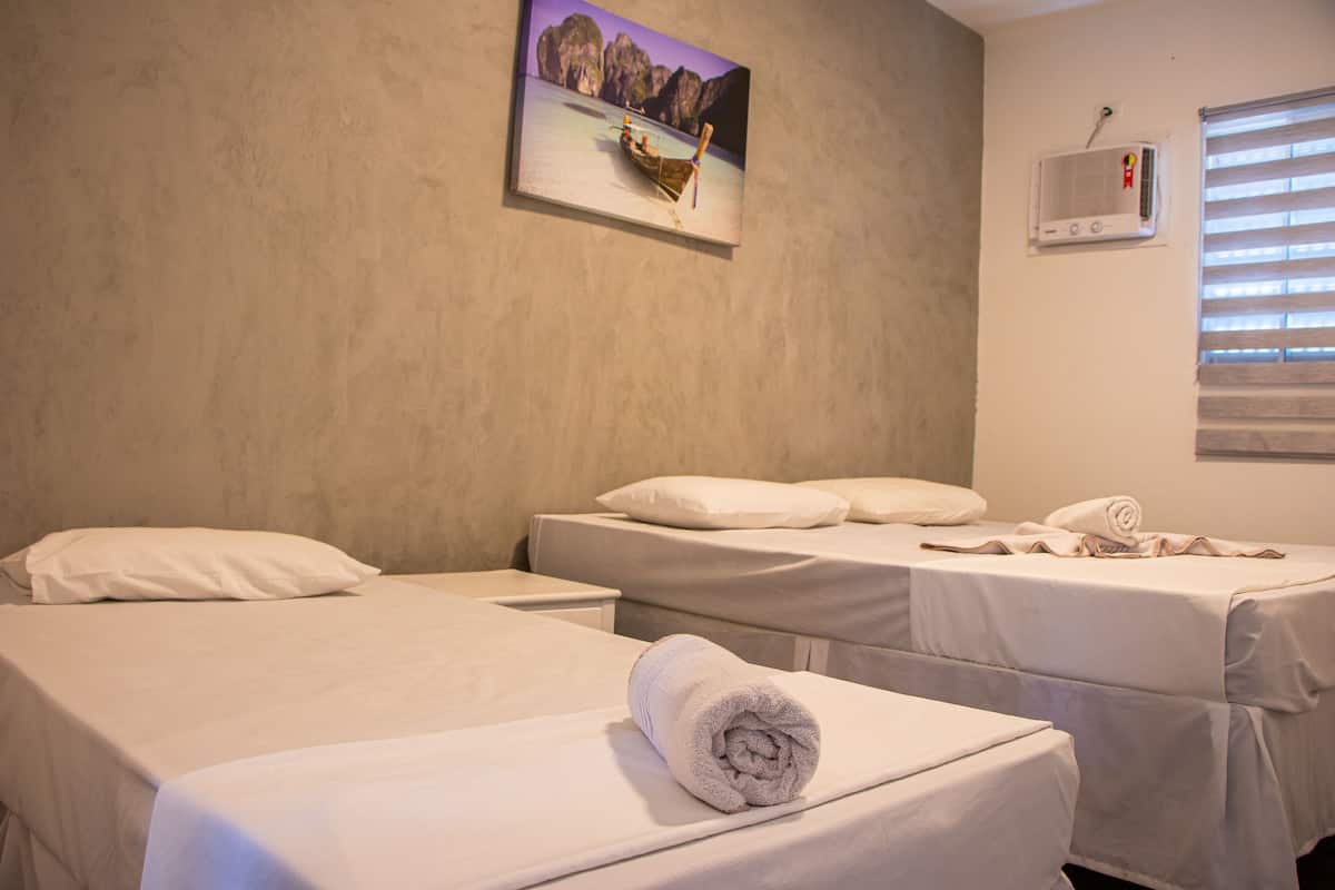 Habitación de hotel con dos camas, un cuadro de un barco en el agua, una ventana con persianas y un aire acondicionado instalado en la pared.