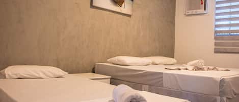 Habitación de hotel con dos camas, un cuadro de un barco en el agua, una ventana con persianas y un aire acondicionado instalado en la pared.
