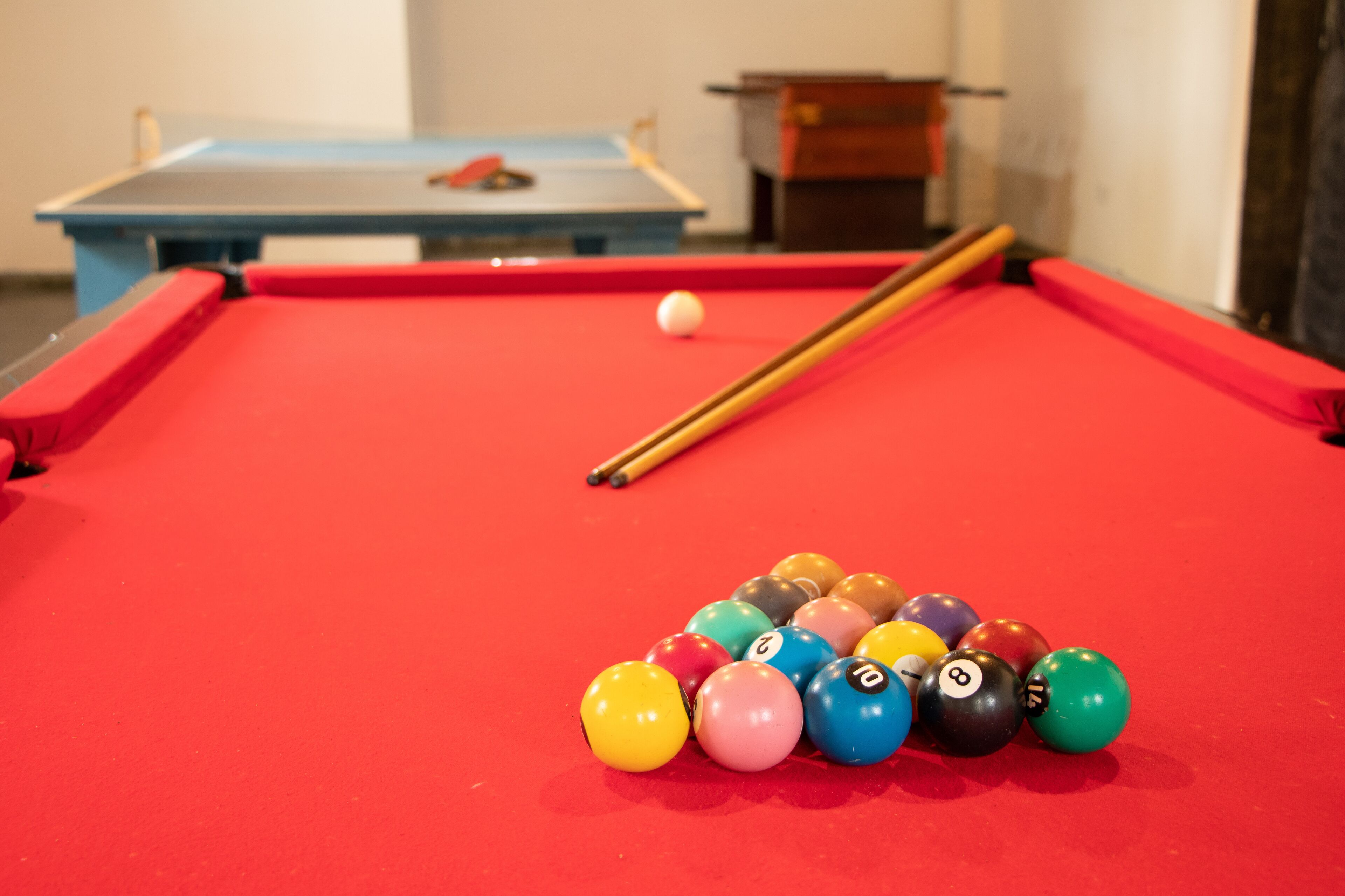 A pool table with a red felt surface, a white cue ball, and a set of numbered pool balls.