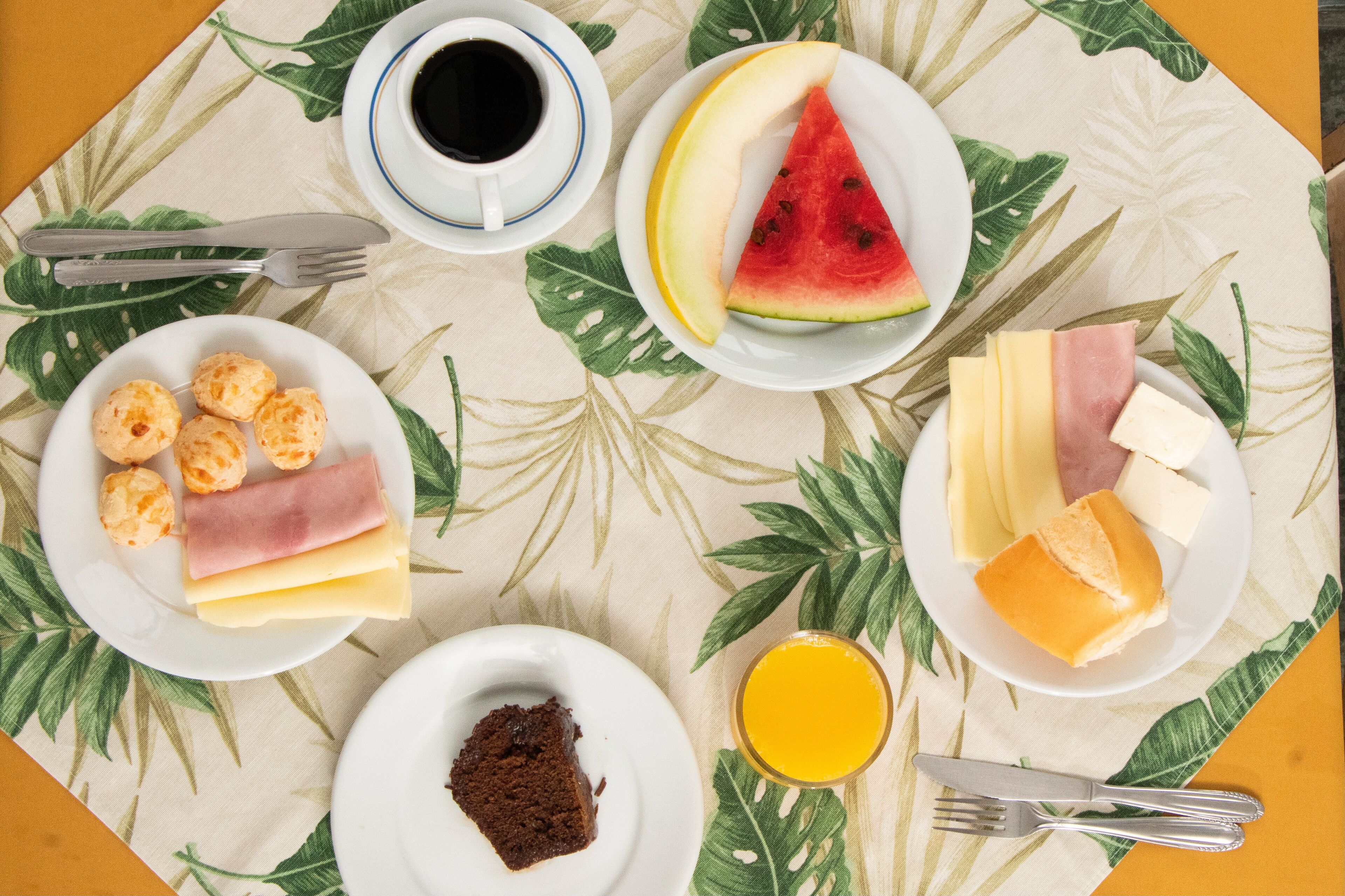 Een ontbijttafel met borden eten, een kop koffie en een glas sinaasappelsap, met een tropisch bladmotief.