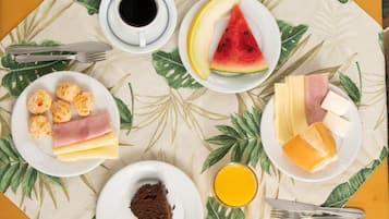 Een ontbijttafel met borden eten, een kop koffie en een glas sinaasappelsap, met een tropisch bladmotief.