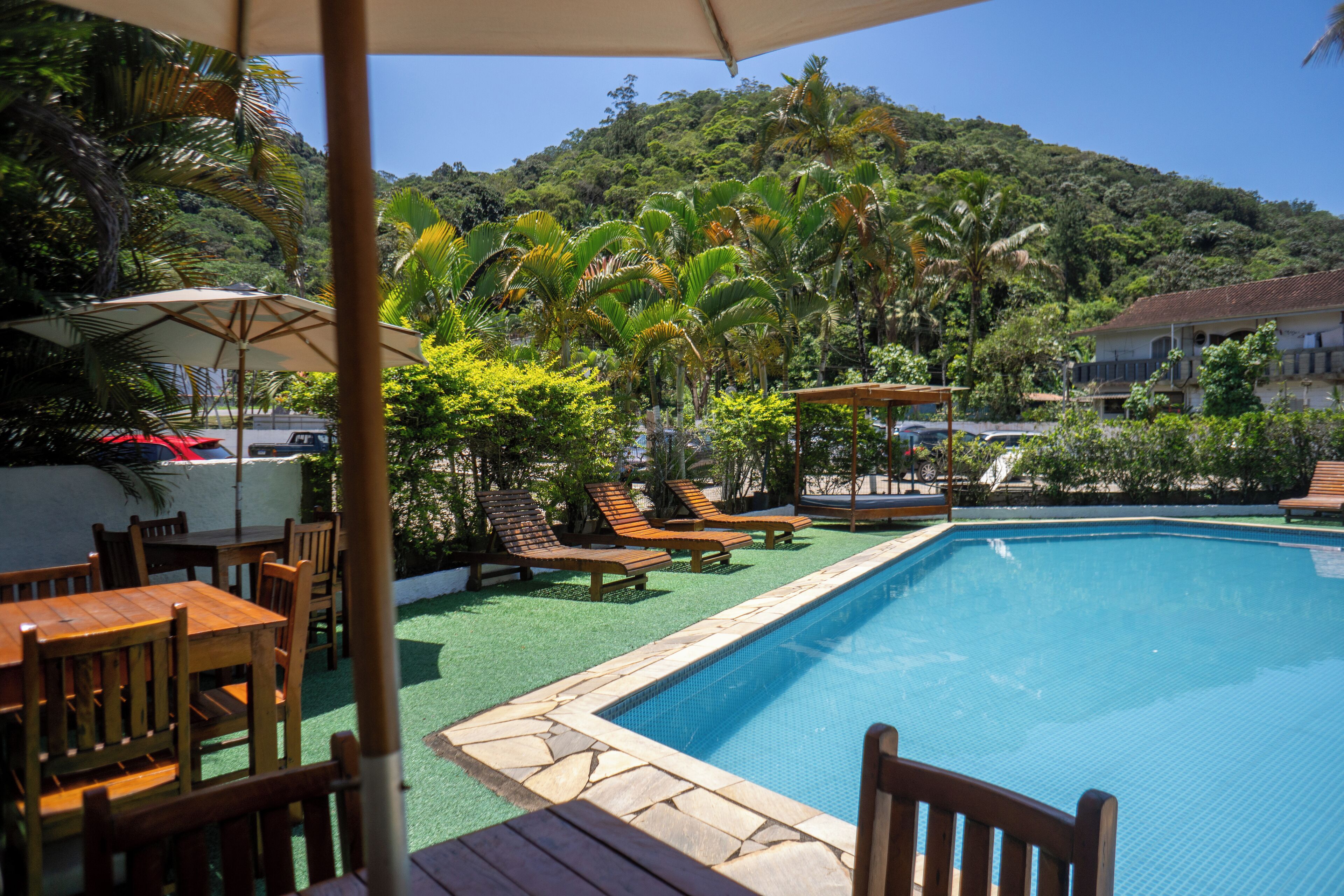 A swimming pool surrounded by wooden furniture and palm trees, with a view of a hill in the background.