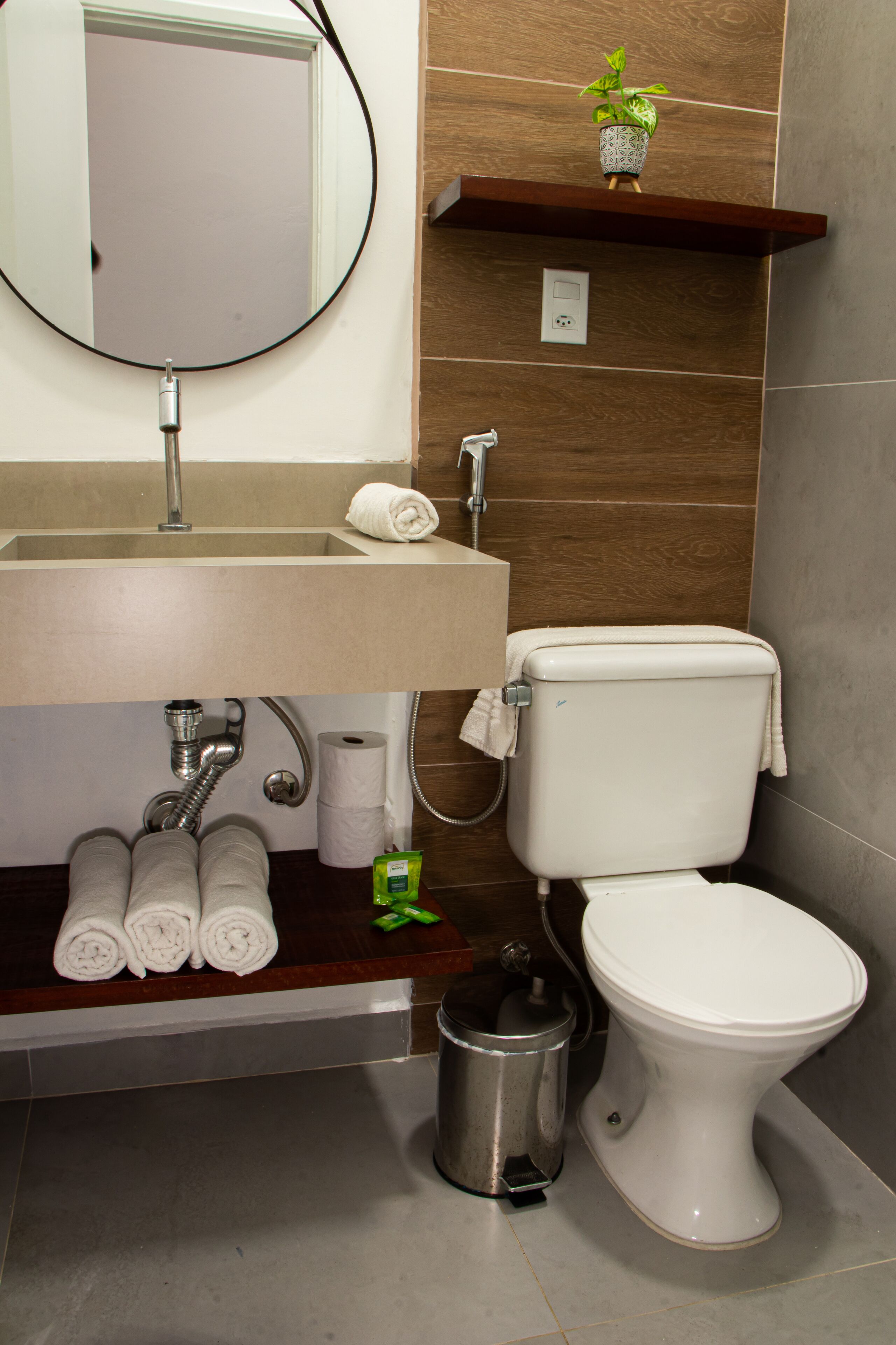 Une salle de bain équipée d’un lavabo, d’un miroir, de toilettes et d’une petite poubelle.