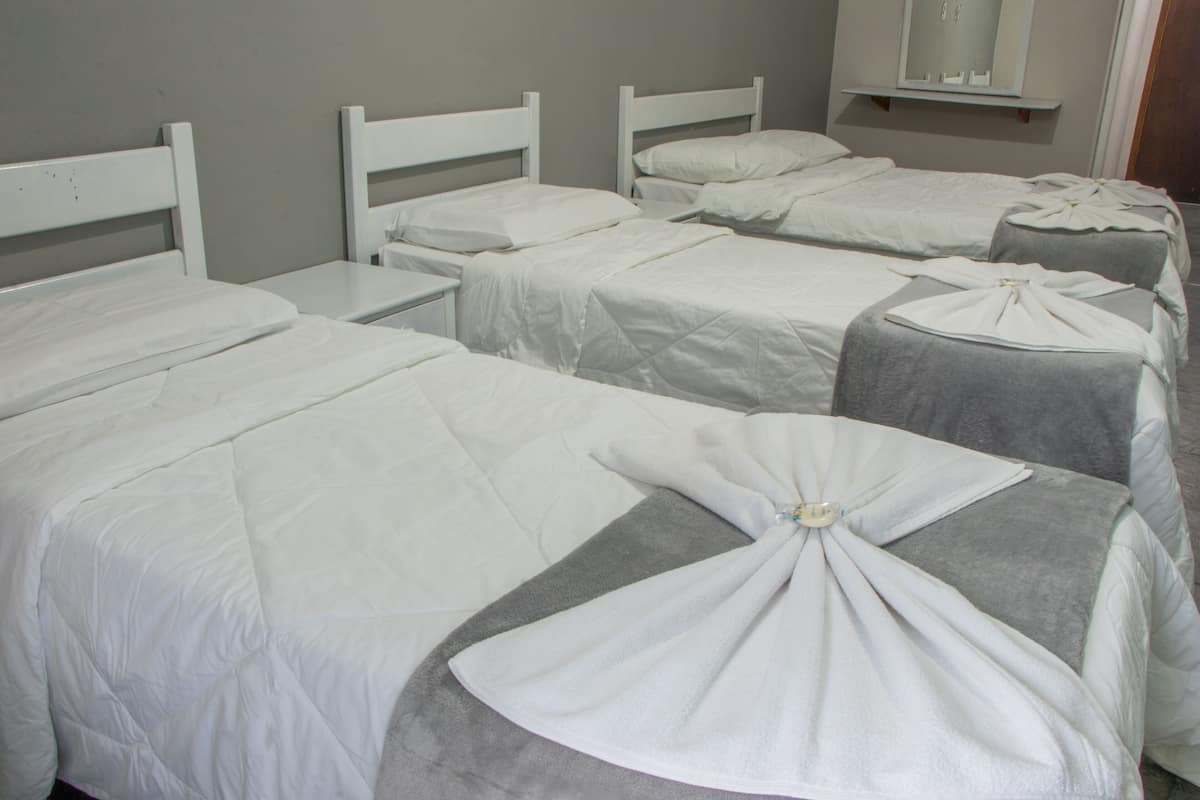 Una habitación de hotel con cuatro camas dispuestas en fila, cada una con ropa de cama blanca y cabeceros.