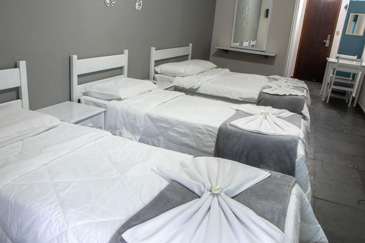 Habitación de hotel con tres camas individuales, una mesita de noche pequeña, un espejo y una puerta.