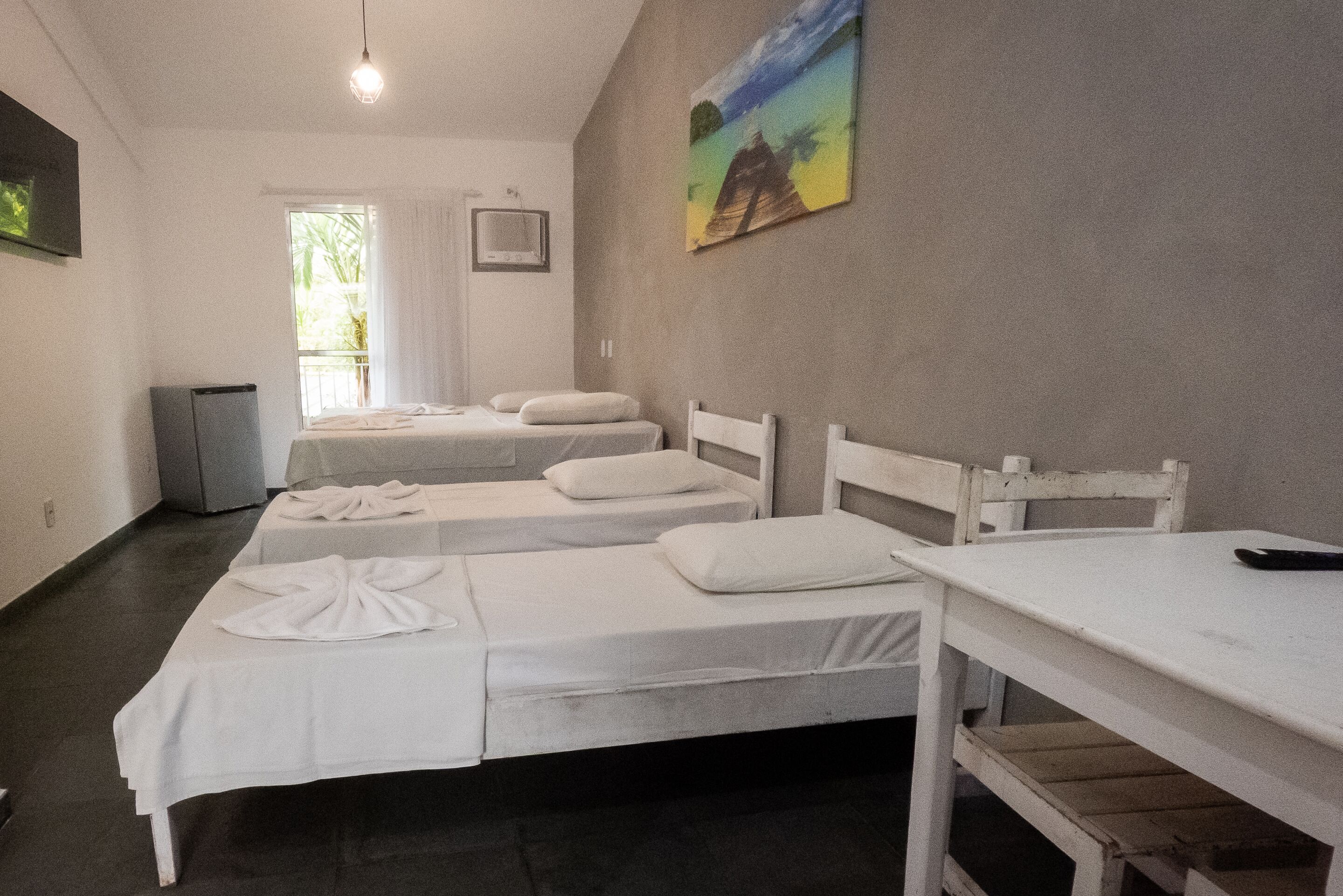 Een kamer met drie eenpersoonsbedden, een tafeltje, een televisie en een schilderij aan de muur.