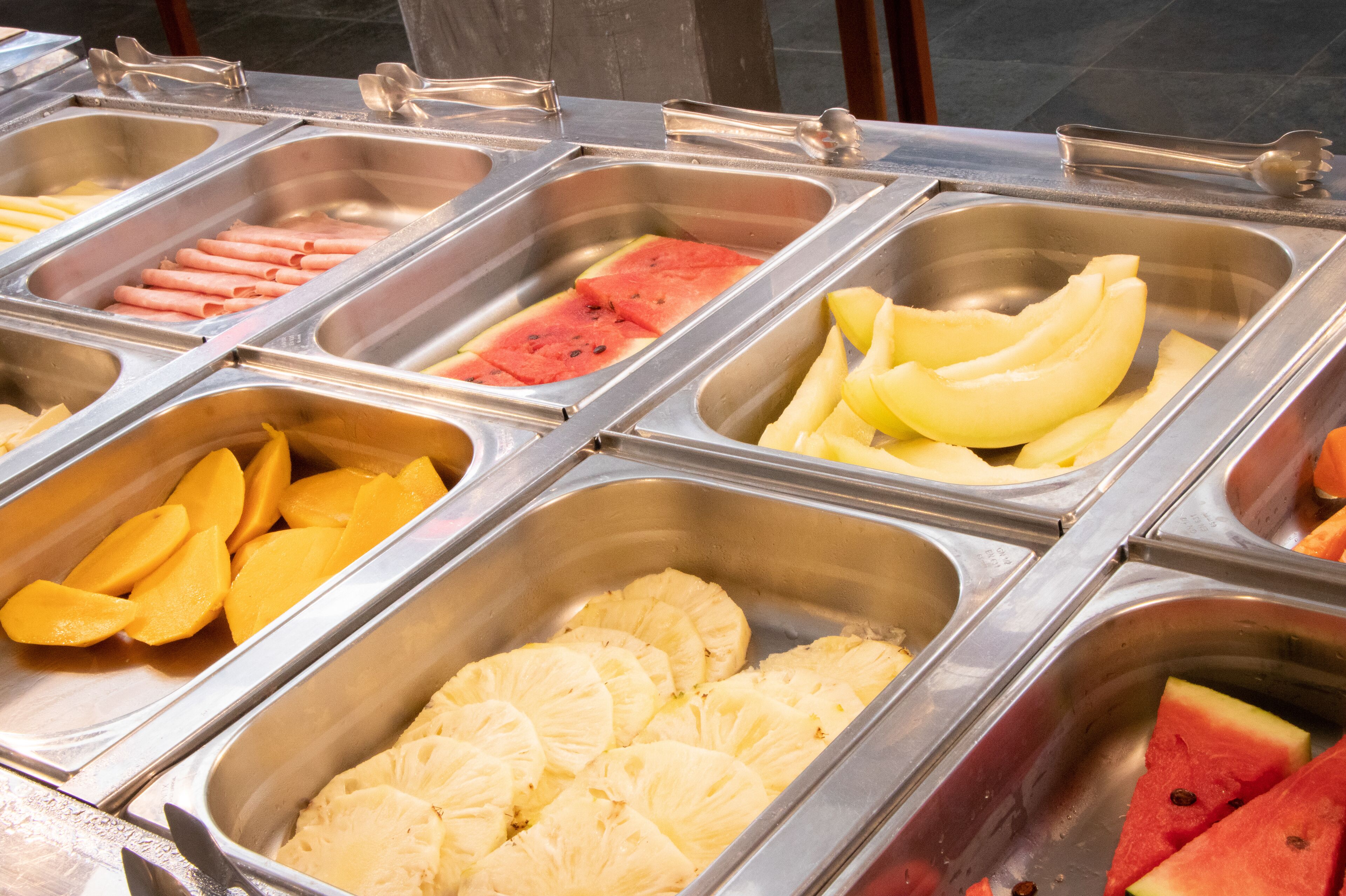 Un bufé con diversas opciones de comida, incluyendo frutas, verduras y carnes.