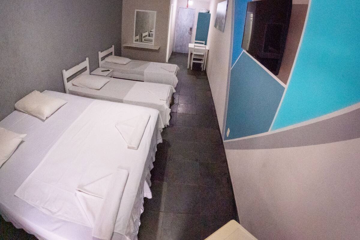 Habitación de hotel con cuatro camas individuales alineadas a lo largo de una pared, un escritorio pequeño y un espejo.