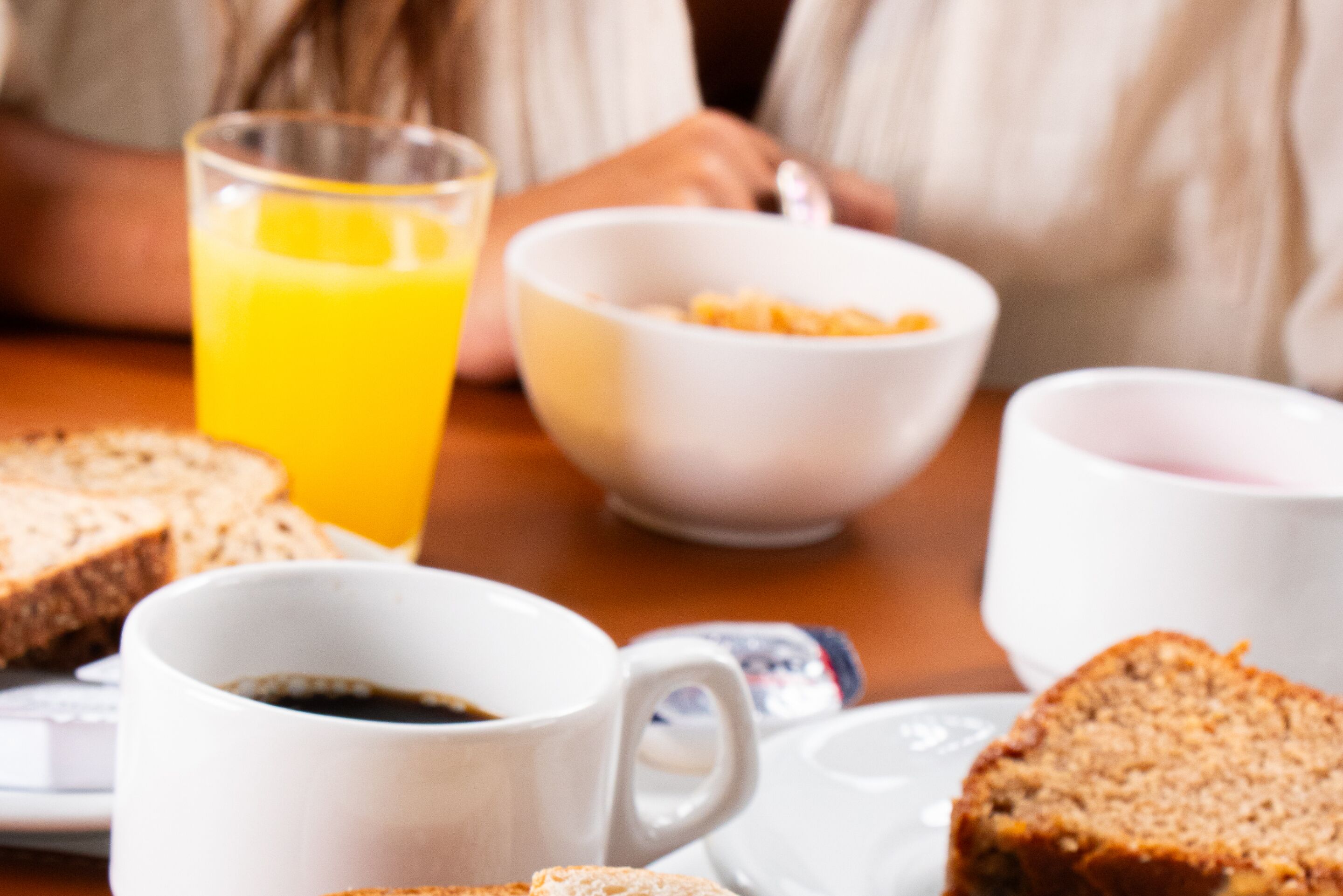A breakfast setting with a bowl of cereal, a glass of orange juice, a cup of coffee, and slices of bread on a table.