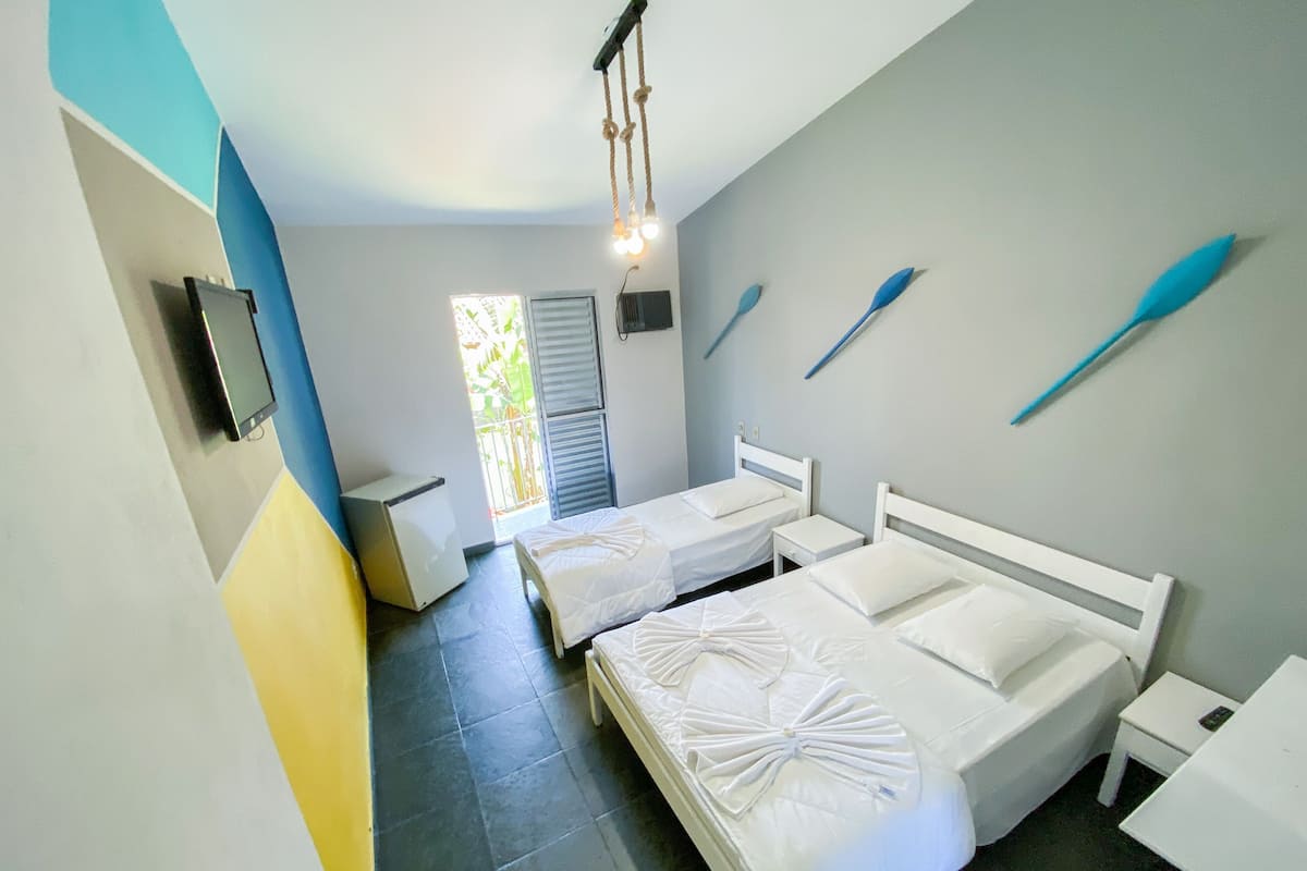 Una habitación de hotel con dos camas, una mesita, un televisor y una ventana con persianas.