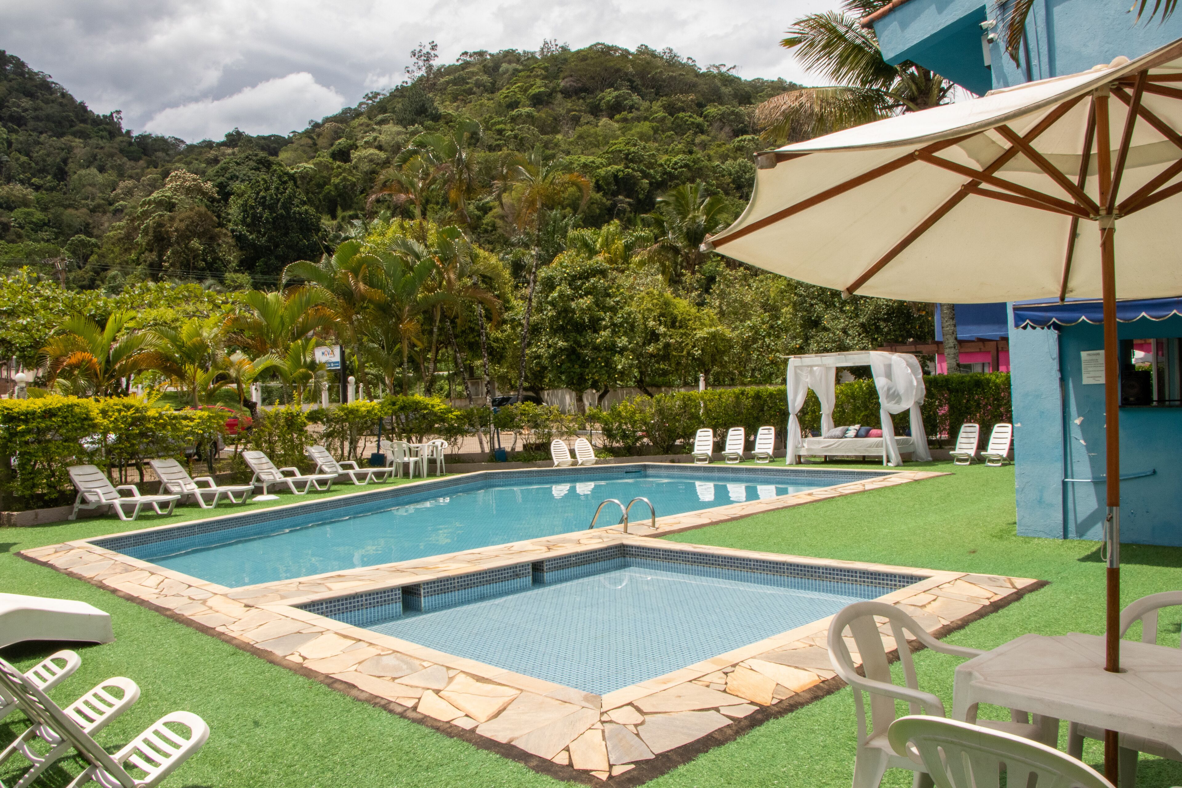 Une piscine entourée de chaises longues et d’une table, le tout agrémenté de verdure et avec une chaîne de montagnes en toile de fond.