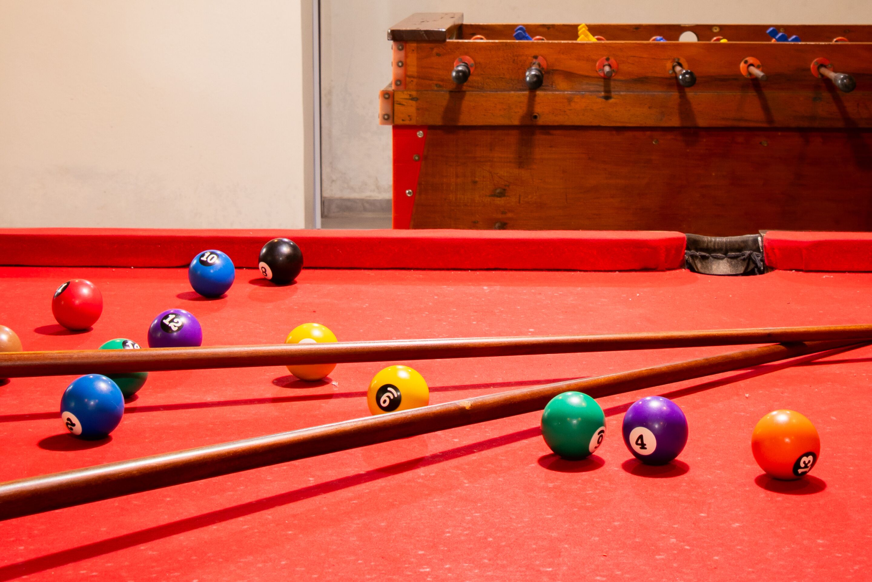 A pool table with balls and cues, and a foosball table in the background.