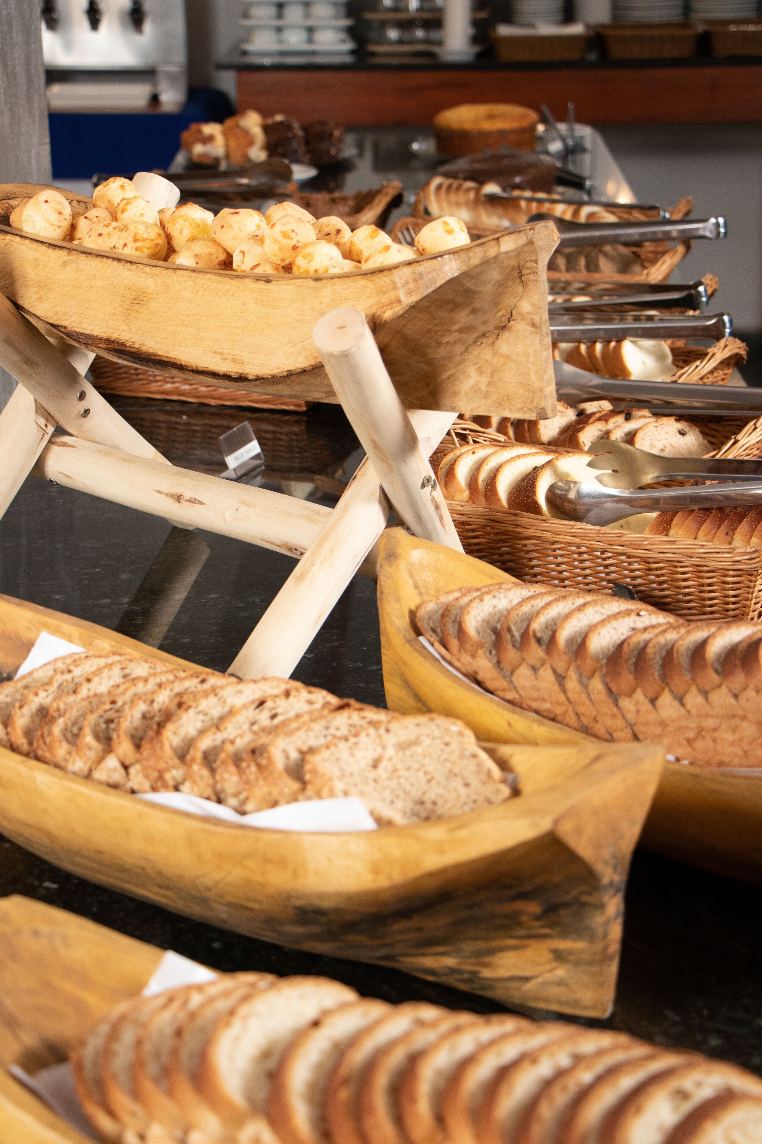 A variety of breads and pastries displayed in wooden bowls and baskets, suggesting a bakery or breakfast setting.