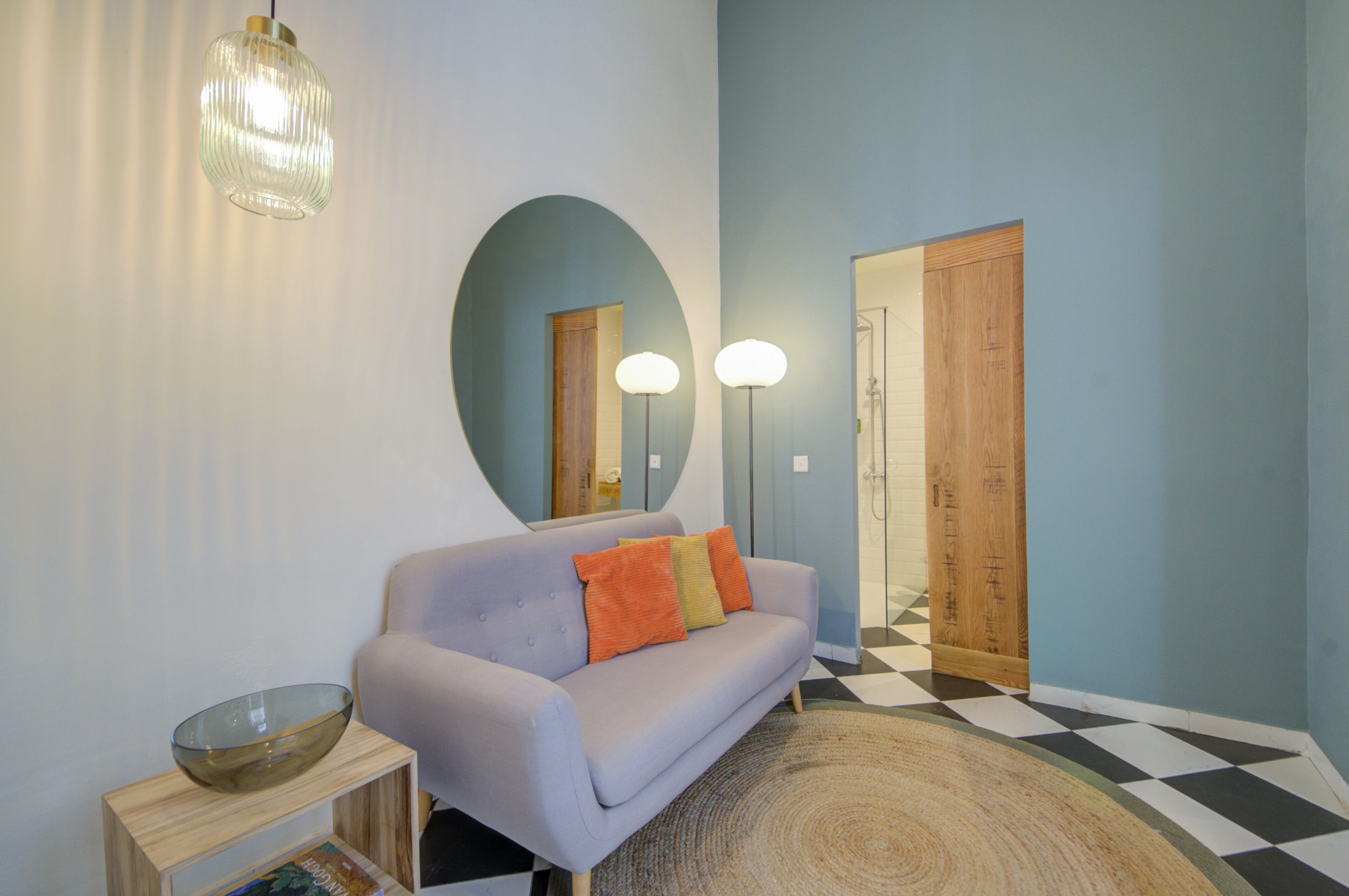 Una sala de estar moderna con un sofá lavanda claro, un cuenco de vidrio sobre una mesita de madera y un espejo grande en la pared.
