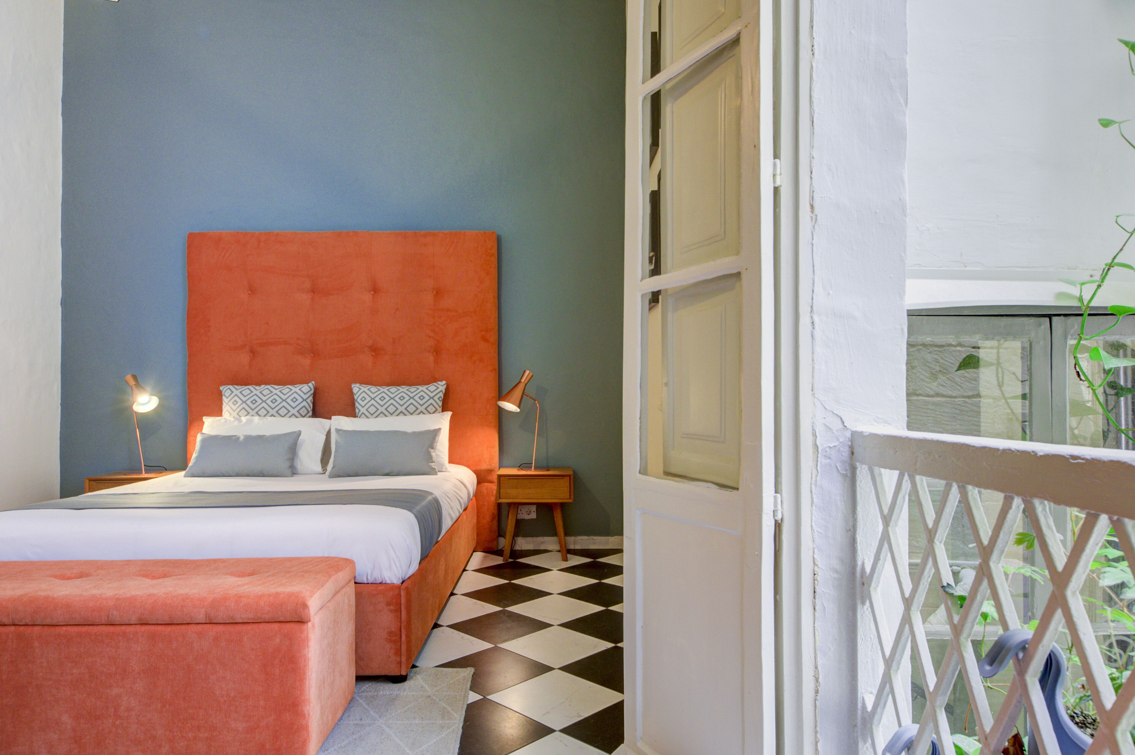A bedroom with a bed, bedside tables, a nightstand, and a window with a view of greenery.