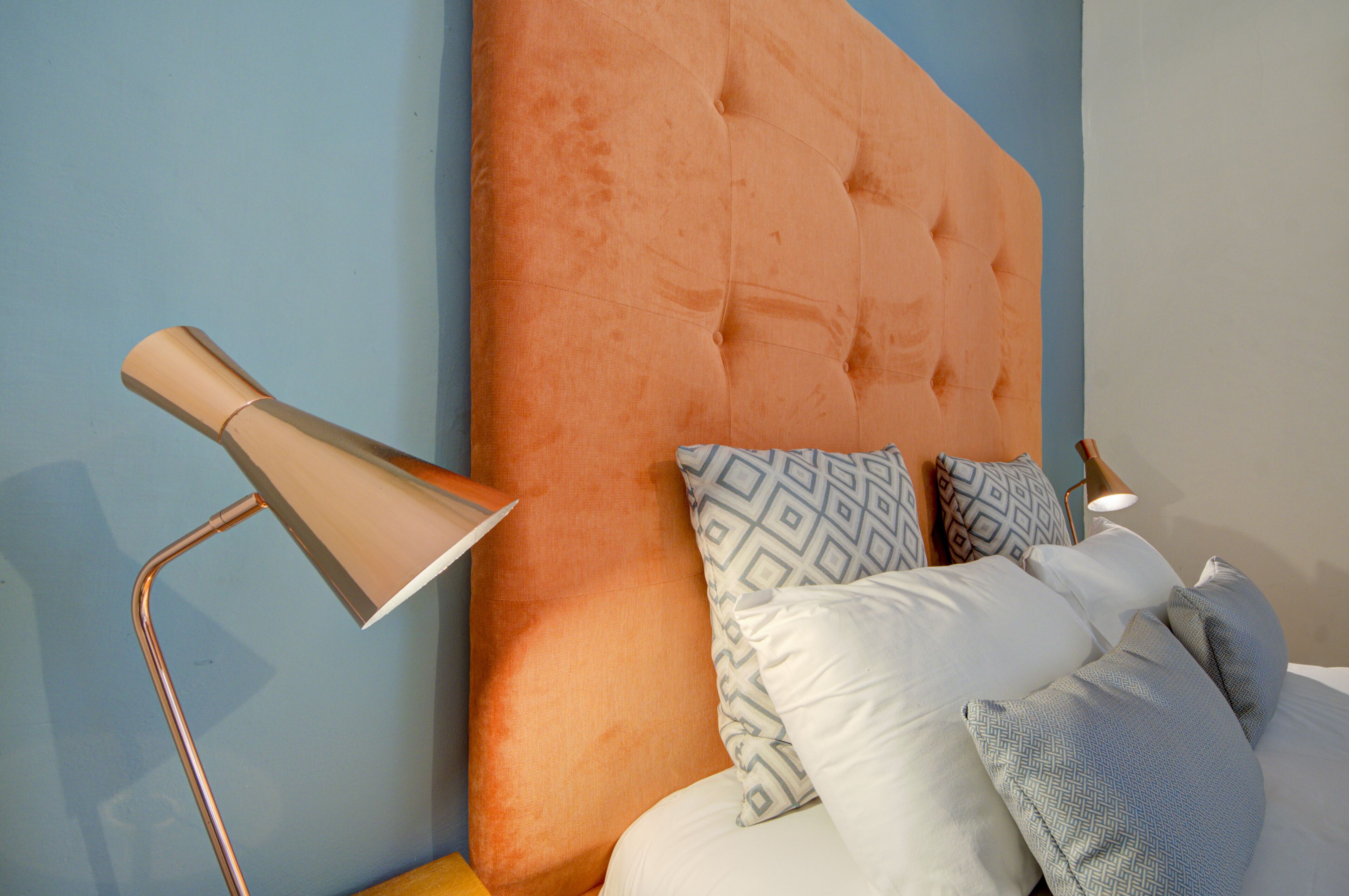 A bed with a tufted headboard, patterned pillows, and a modern floor lamp.