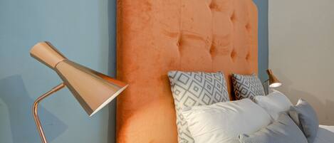 A bed with a tufted headboard, patterned pillows, and a modern floor lamp.