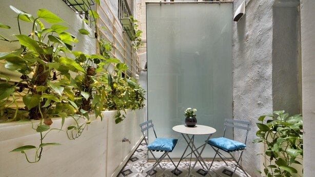 A small, enclosed patio area with a tiled floor, two folding chairs with blue cushions, a small table, and potted plants.