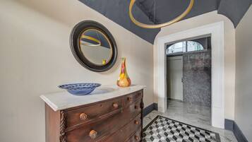 Une salle de bain avec un sol en marbre, une commode en bois, un bol bleu, un vase et un miroir.
