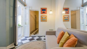 A living room with a checkered floor, a sofa with colorful cushions, and framed pictures on the wall.