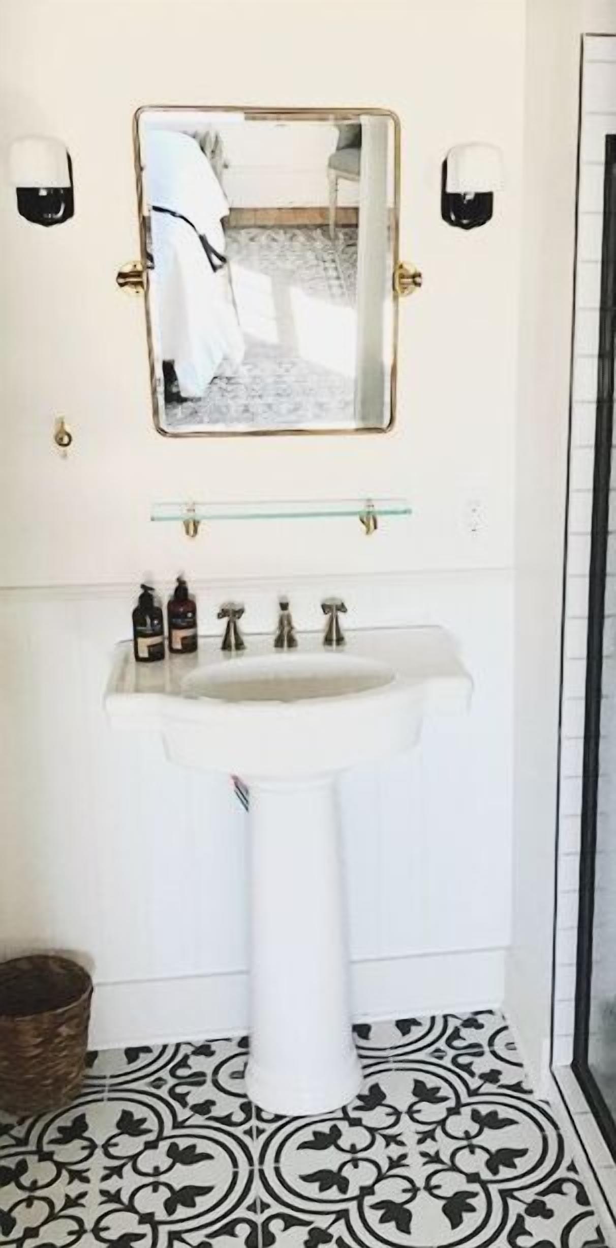 Un baño con un lavamanos pedestal blanco, un espejo encima y dos luces fijadas a la pared.