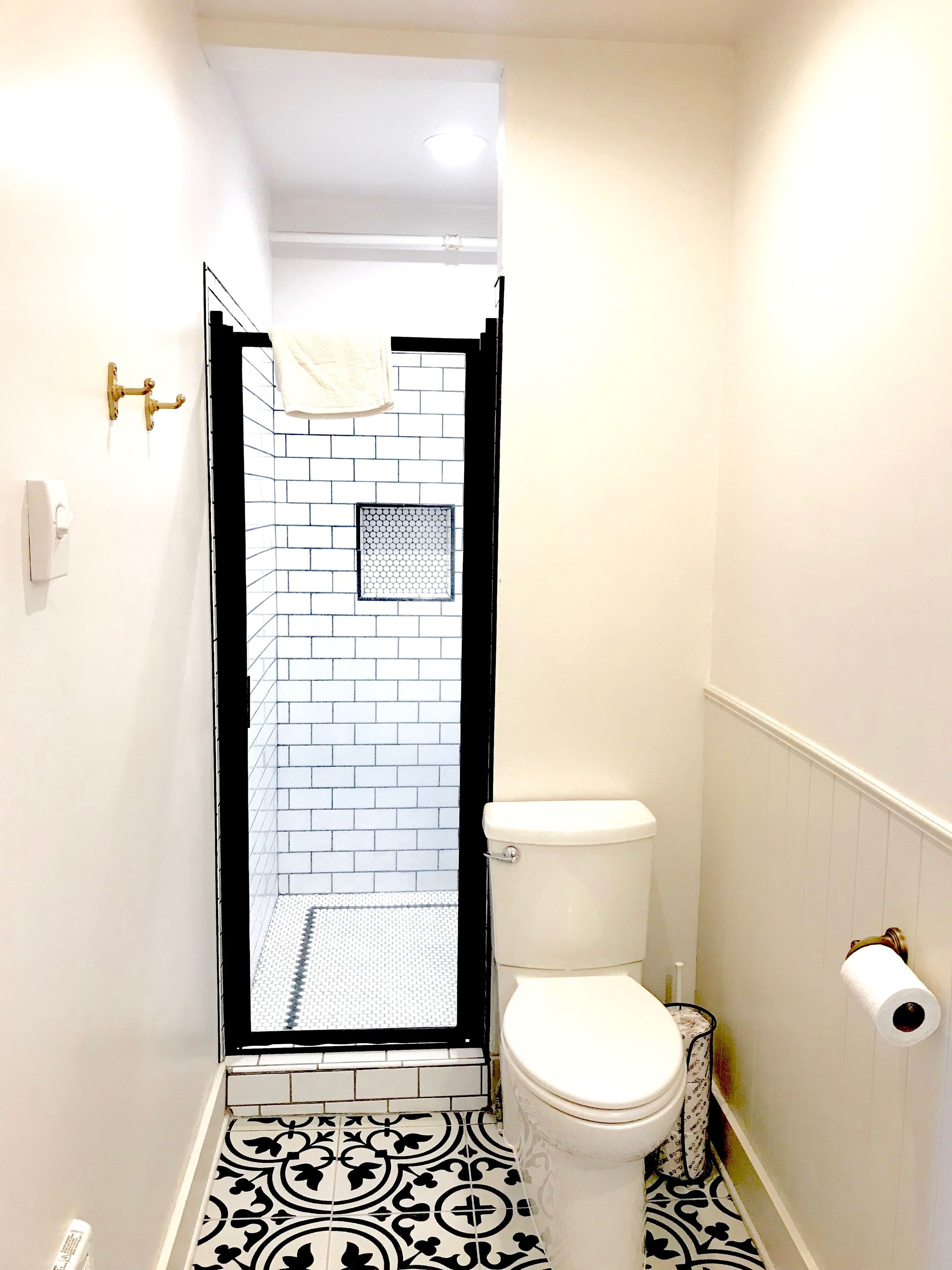 A bathroom with a white toilet, a shower with a black frame, and a patterned floor.