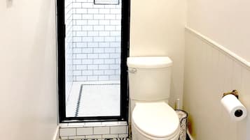 A bathroom with a white toilet, a shower with a black frame, and a patterned floor.