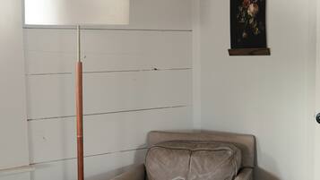 A corner room with a chair and ottoman, a floor lamp, and a framed picture on the wall.