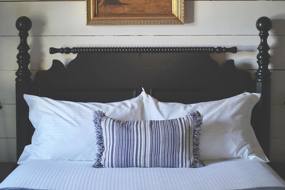 A bed with white and striped bedding, a dark wooden headboard, and a framed picture above.