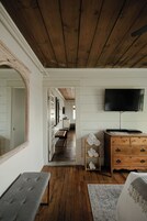 Una habitación con techo de madera, un espejo grande, un banco, un televisor y un aparador de madera con cajones.