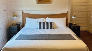A wooden-paneled bedroom with a large bed, two bedside tables with lamps, a hanging light fixture, and a framed picture on the wall. - The Landing Hotel and Dining (La Grande)