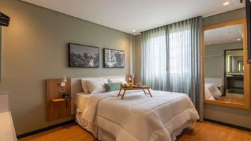 Habitación de hotel con una cama grande, mesitas de noche, una lámpara de noche, una bandeja con alimentos para el desayuno y un espejo amplio.