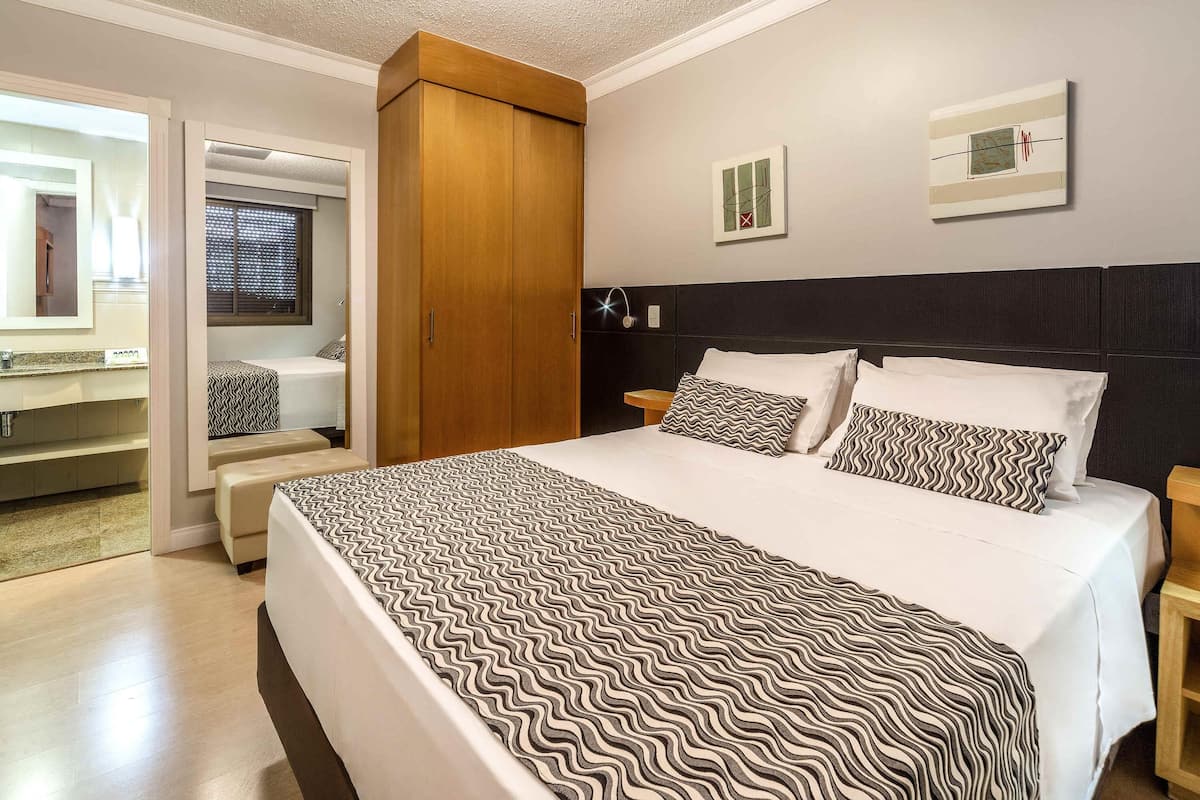 Un dormitorio con una cama grande, un armario de madera y un baño visible a través de una puerta abierta.