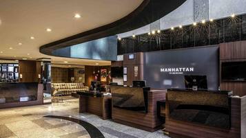 Un hall de hotel con mostrador de recepción, zona de estar y una pantalla grande que muestra el nombre del hotel.