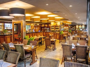 A restaurant with multiple dining tables and chairs, a bar area, and a kitchen visible in the background.
