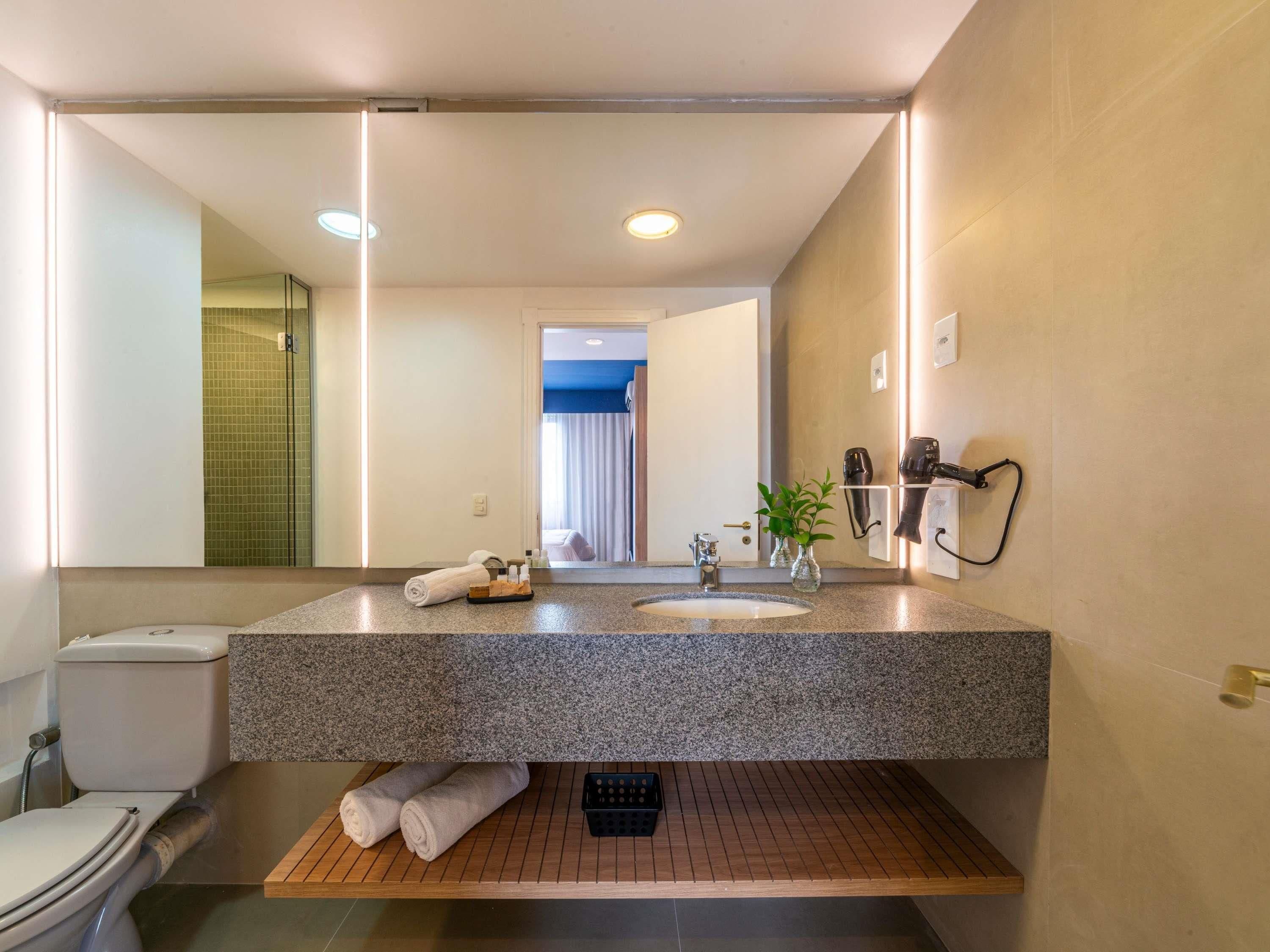 Un baño moderno con encimera de granito, un lavabo, un inodoro, un espejo y una zona de ducha.