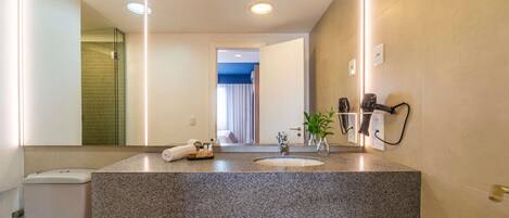 Un baño moderno con encimera de granito, un lavabo, un inodoro, un espejo y una zona de ducha.