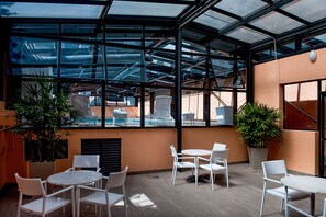 A covered outdoor area with tables and chairs, large potted plants, and a view of a swimming pool through the glass roof. - Manhattan Porto Alegre by Mercure (Porto Alegre)