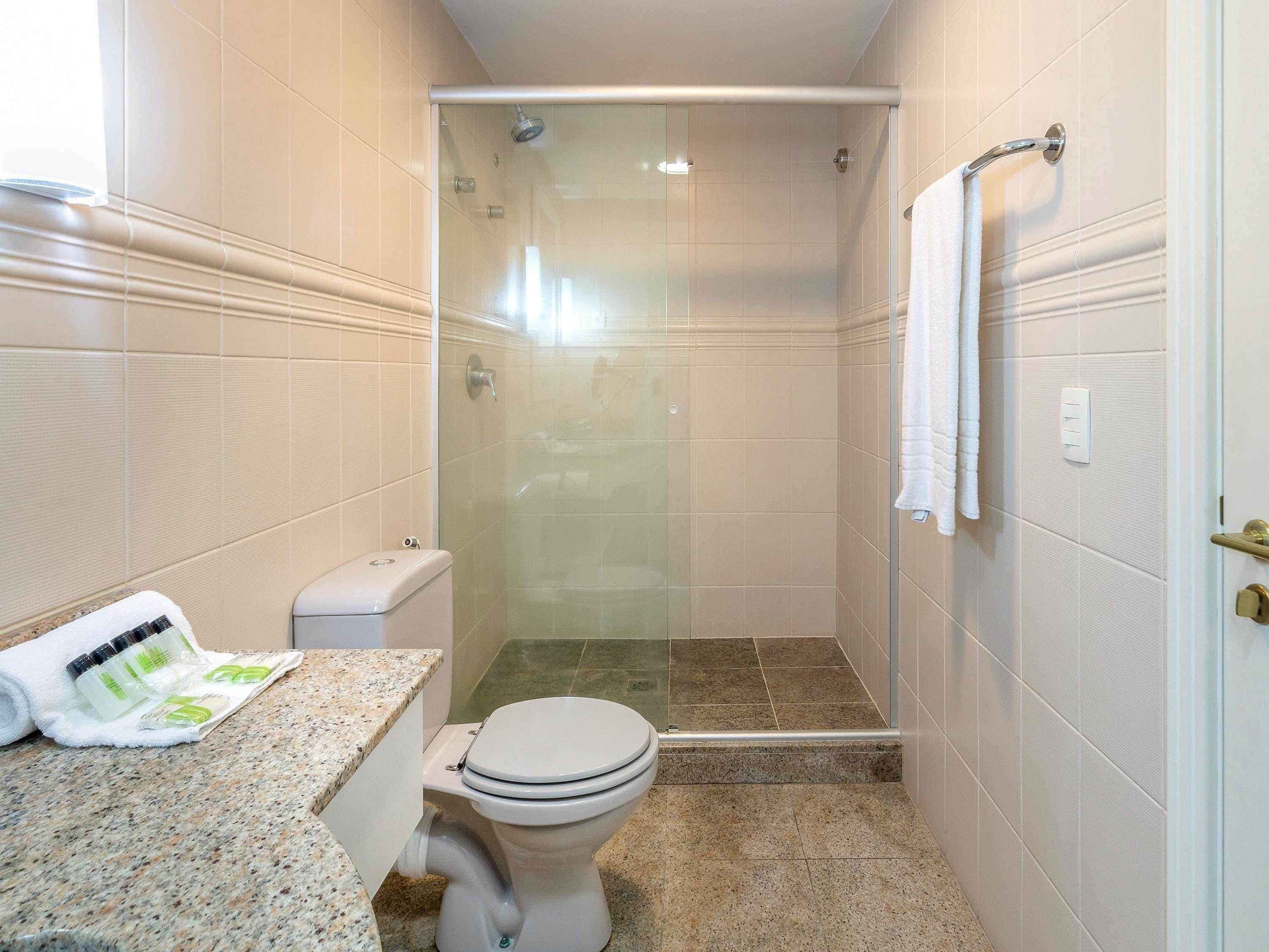 A bathroom with a toilet, shower, and granite countertop.