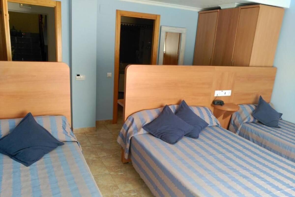 Un dormitori amb dos llits, cadascun amb roba de llit de ratlles blaves i almoines fosques. Hi ha un armari de fusta i una porta que dona a una altra habitació.