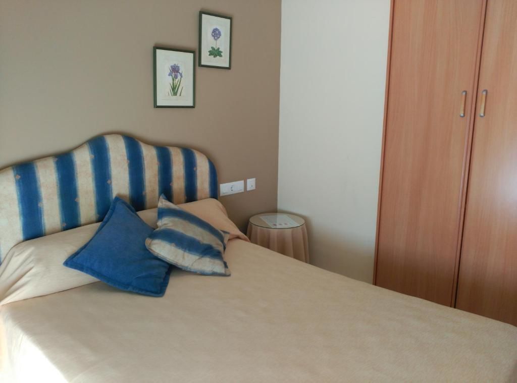 Un dormitorio con cabecera a rayas, cama con ropa de cama azul y beige, dos cuadros con motivos florales en la pared y un armario de madera.