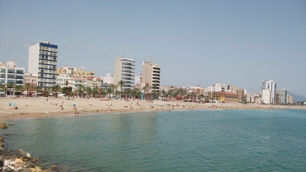 Un paisaje urbano costero con una playa arenosa, aguas azules cristalinas y diversos edificios, incluyendo apartamentos de gran altura y hoteles.