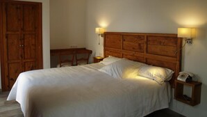 Un dormitorio con cabecera de madera, dos lámparas de noche, un teléfono en la mesita y un armario de madera.